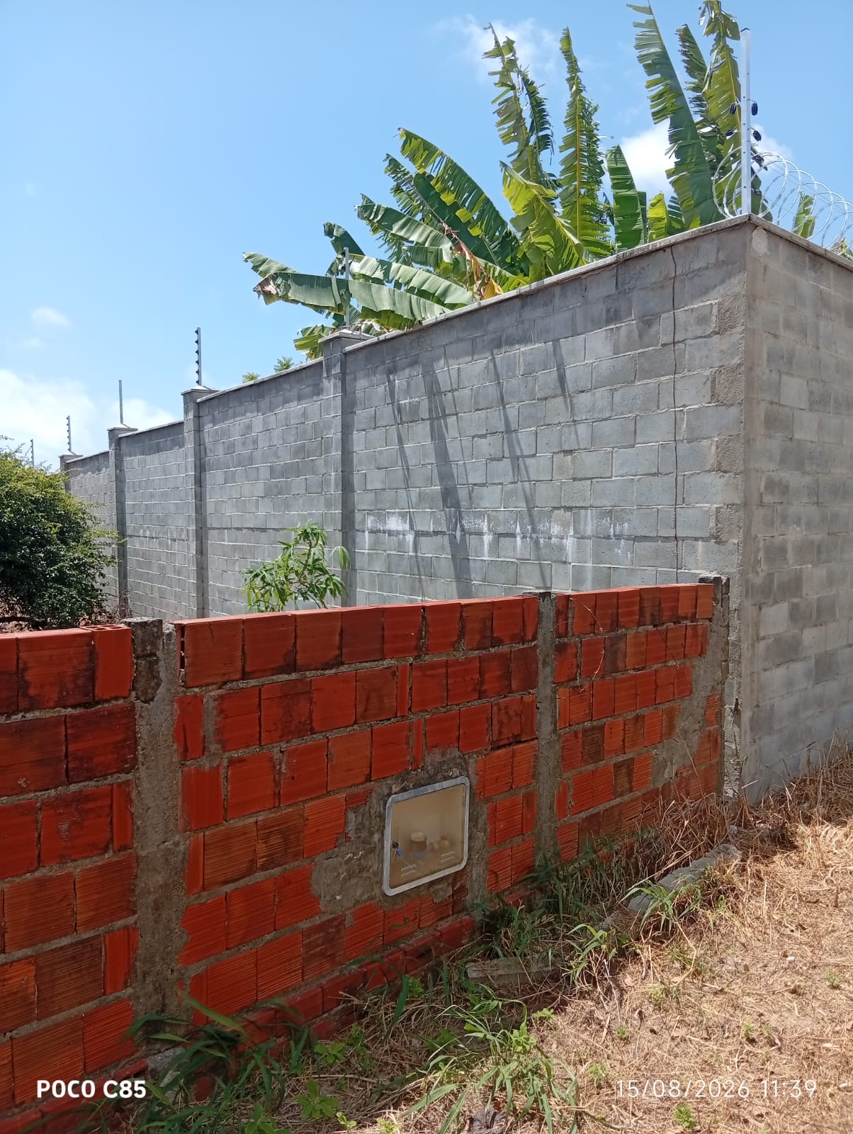Muro de bloco com cerca elétrica no topo, instalação em residência com vegetação ao fundo